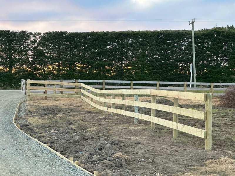 A curved post and rail fence following a driveway and meeting an older fence at a gate