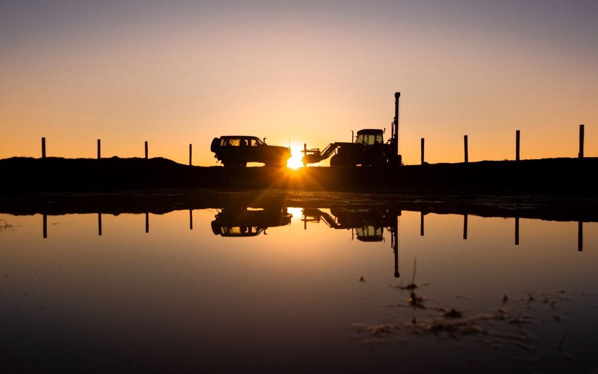 The ute and tractor-mounted post driver against a Canterbury sunset, mirrored in water