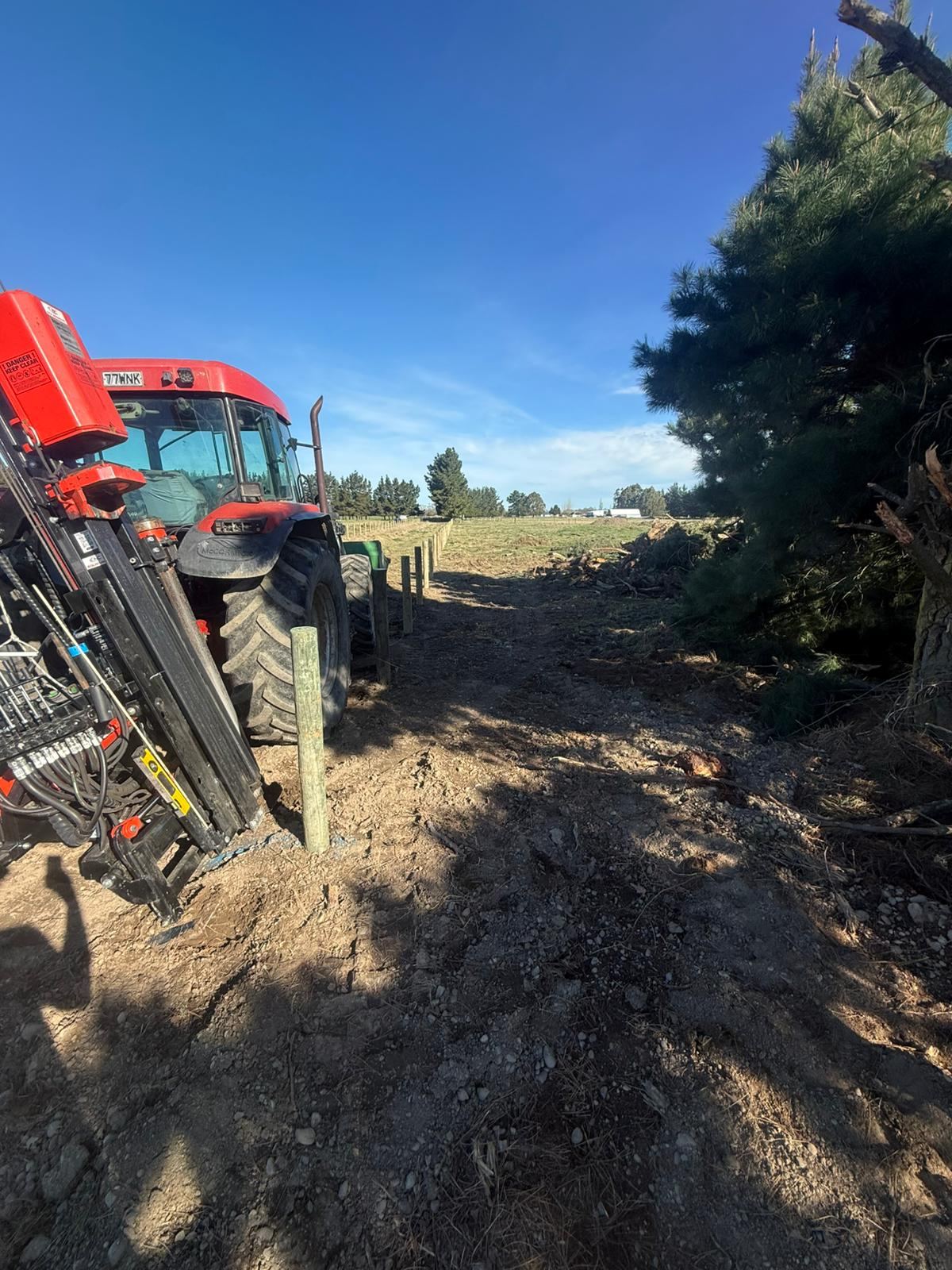 The tractor and post driver setting a timber post, a line of posts already standing behind