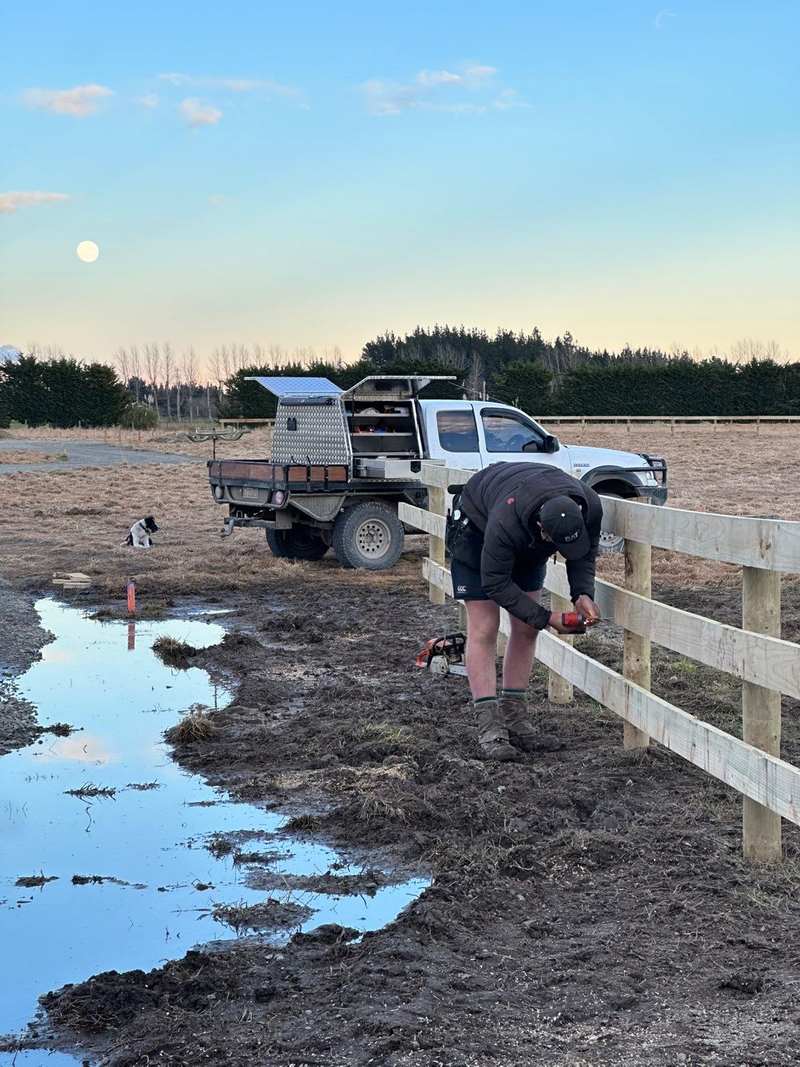 Nathan fixing a rail on a new fence at dusk, ute and dog behind him